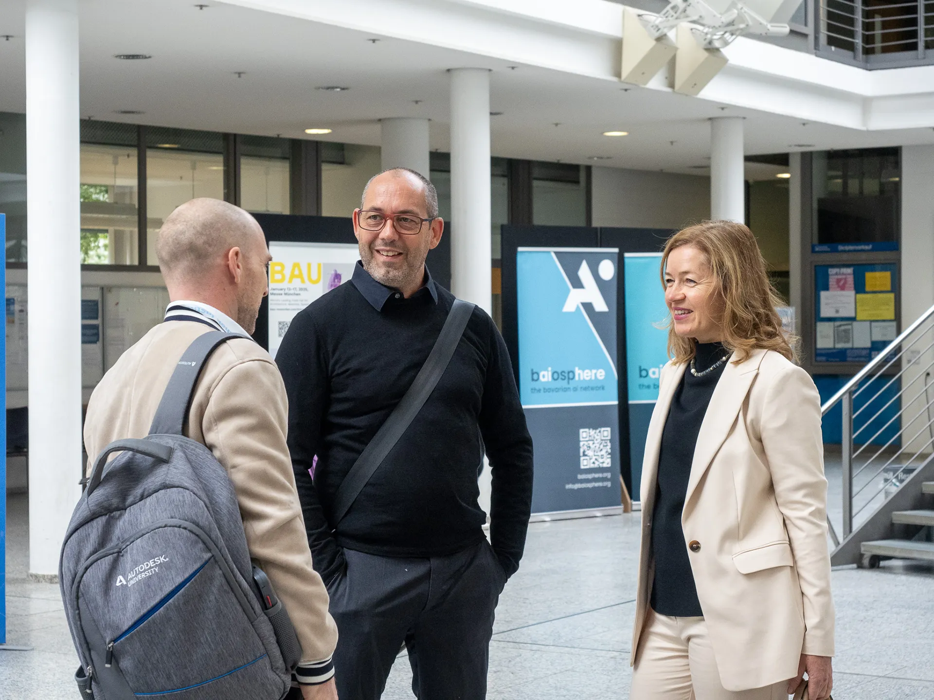 Zwei Männer (links) und eine Frau (rechts) unterhalten sich vor BAIOSPHERE Roll-ups im Hintergrund